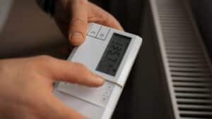 Persona ajustando la temperatura de un termostato digital de aerotermia junto a un radiador.
