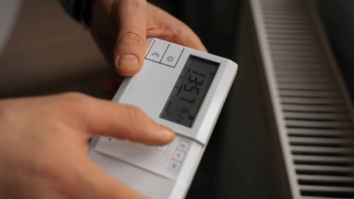 Persona ajustando la temperatura de un termostato digital de aerotermia junto a un radiador.